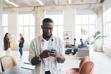 Serious ethnic man using smartphone in office