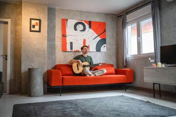 One man adult Caucasian sit at home on sofa bed in room play guitar