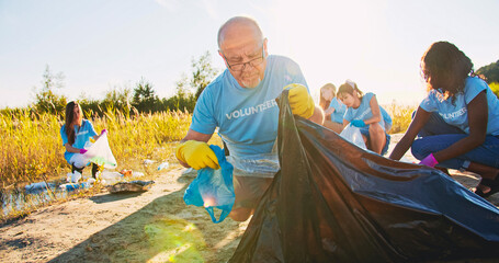 A senior volunteer cleaning up the beach from pollution. a male eco protector picking up garbage,...