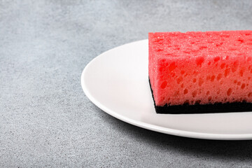 Red viva magenta sponge for dishwashing on a white plate on a neutral gray background. Gentle dishwashing. House cleaning