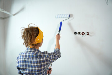 Positive overjoyed woman painter holding roller painter painting walls in room. People renovation...