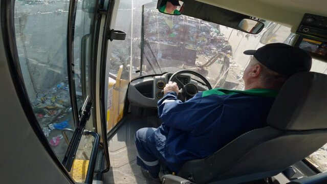 Man driving a front loader, grabbing a waste with a scrap handling grapple bucket and transferring it to the heap, cabin view.
