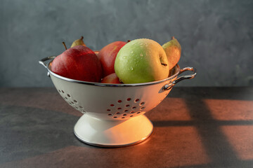 Colander with washed fruits on a wooden table, sunlight through the window.