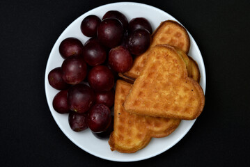 Delicious waffles and grapes on a plate. A sweet breakfast of waffles and red grapes. Heart-shaped waffles.