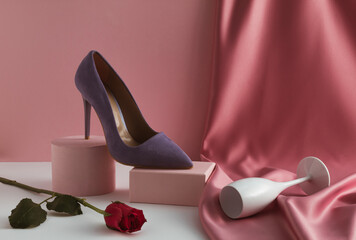 Contemporary composition with elegant woman high heel purple shoe on product podium, rose flower, champagne glass and pastel pink silk curtain. Valentine's Day or 8 March beauty concept.
