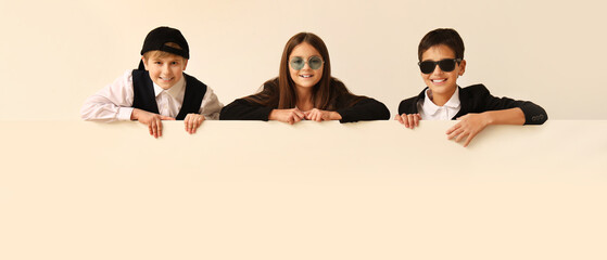 Little friends in stylish clothes and with blank poster on light background