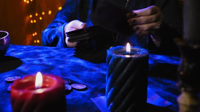 A fortune teller at a table in candlelight reads the future from tarot cards on black velvet with blue highlights. Medium plan