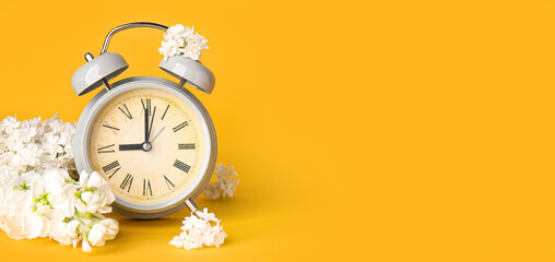Alarm clock and flowers on orange background with space for text. Spring time