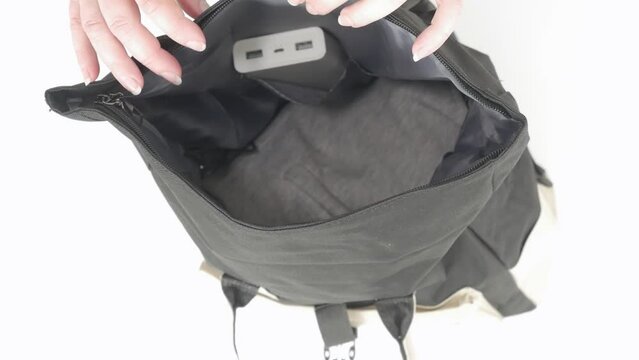 Top view female hands fold in black travel backpack white power bank