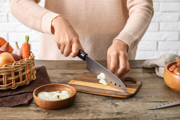 Woman cutting fresh onion on wooden table in kitchen