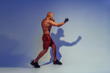 Fototapeta na wymiar Professional kickboxer is training and practicing punch on studio background with shadows
