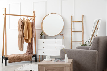 Interior of stylish dressing room with mirror, clothes and drawers