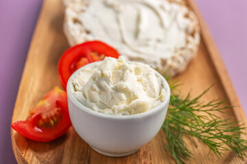 Bowl of tasty cream cheese on color background, closeup