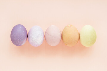 Pastel colored Easter eggs on peach background, top view.