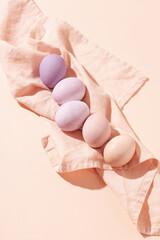 Pastel colored Easter eggs lying on linen napkin on peach background. Minimal styled painted eggs in hard light.