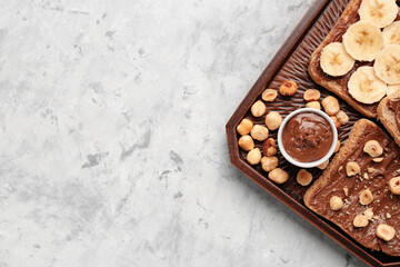 Wooden board of tasty toasts with hazelnut butter, banana and nuts on light background