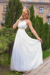 blonde beautiful natural girl with blonde hair in a white dress in nature, on the street, in the garden by a tree, with makeup and hairstyle, greek woman in a white ethnic historical dress, retro