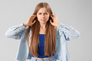 Young woman suffering from loud noise on grey background