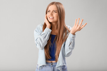 Young woman suffering from loud noise on grey background
