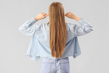 Young woman suffering from loud noise on grey background, back view