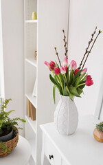 Vase with tulips and willow branches on table in living room