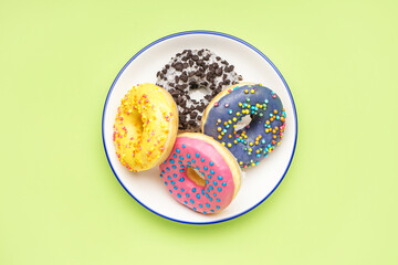 Plate with different delicious donuts on green background