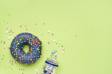 Delicious donut and overturned jar of sprinkles on green background