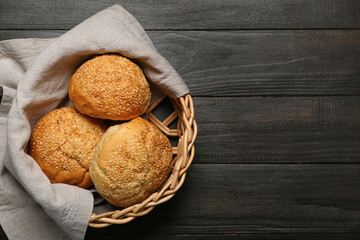 Delicious buns with sesame seeds in wicker basket on black wooden background