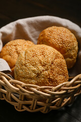 Delicious buns with sesame seeds in wicker basket on black wooden background