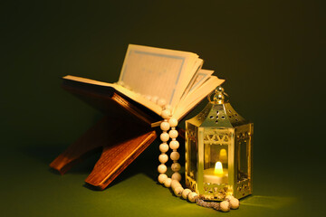 Muslim lantern with candle, Koran and prayer beads for Ramadan on green background