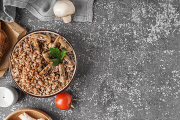 Bowl of tasty buckwheat porridge with mushrooms, parsley and fresh tomato on grey table