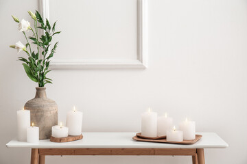 Fototapeta na wymiar Burning candles and vase with eustoma flower on end table near white wall