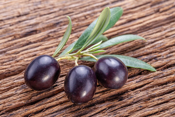 Fresh black olives on olive twig on old wooden background.