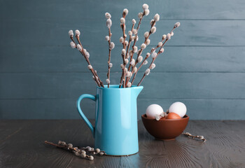 Blue jug with pussy willow branches and Easter eggs on wooden table