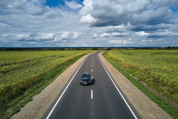 Aerial view of intercity road between green agricultural fields with fast driving car. Top view from drone of highway traffic