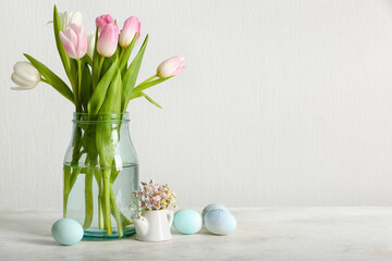 Vase with beautiful tulip flowers and Easter eggs on light background