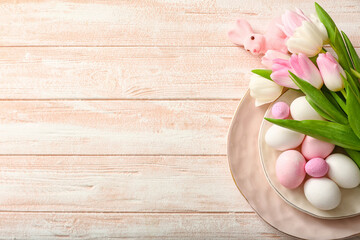 Plate with Easter eggs, tulip flowers and bunny on light wooden background