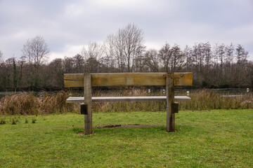 Fototapeta premium empty wooden bench in park facing lake. A lonely bench during cold winter day. 