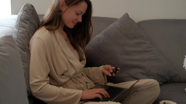Young woman sitting on sofa at home making online payment with laptop and credit card