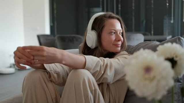 Happy young woman enjoying listening to music in headphones while sitting on sofa at home