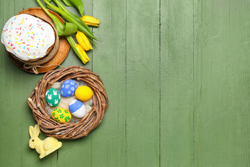 Nest with painted Easter eggs, cake, bunny and tulip flowers on color wooden background