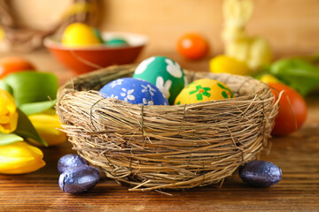Nest with painted Easter eggs, candies and tulip flowers on wooden table, closeup