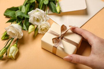 Beautiful eustoma flowers and female hands with gift box for Women's Day celebration on beige background