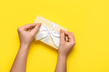 Female hands with gift box for Women's Day celebration on yellow background