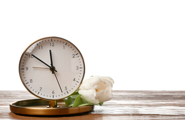 Alarm clock and beautiful tulip on wooden table against white background