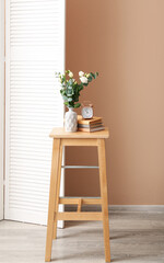 Bouquet of beautiful flowers, books and alarm clock on wooden stool near color wall