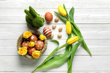 Nest with beautiful Easter eggs, flowers and bunny on light wooden background