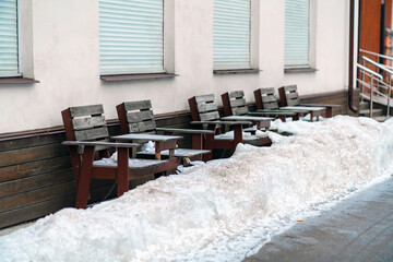 Wooden tables and chairs of an outdoor cafe under a layer of snow and ice