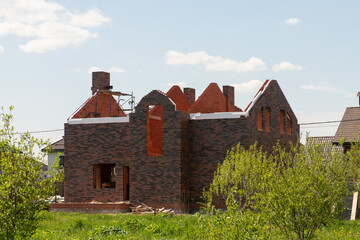Fototapeta na wymiar Facade of new brick house without roof during construction among green landscape