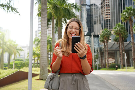 Young businesswoman using phone when walking outside office - Powered by Adobe
